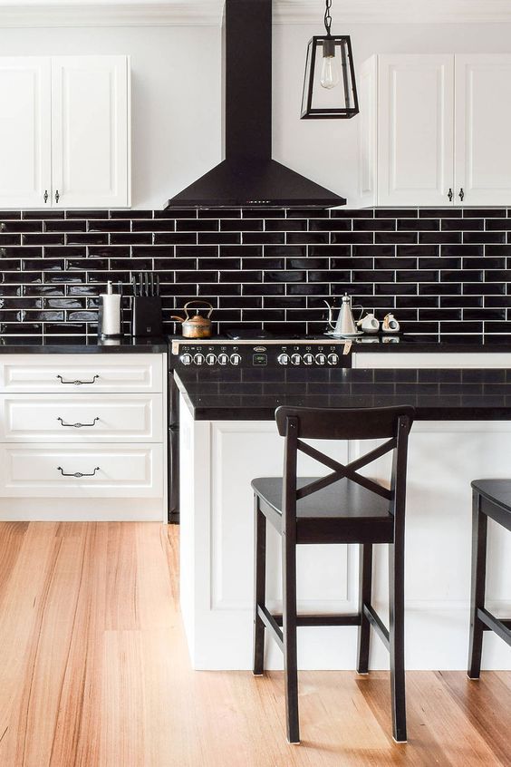 a modern farmhouse kitchen with white shaker cabinets and a kitchen island, black countertops, a black skinny tile backsplash and a black hood