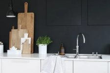 a monochromatic minimalist kitchen with black walls, white cabinetry and white countertops, a black sconce and shiny metal fixtures