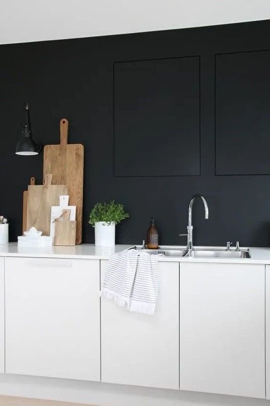 a monochromatic minimalist kitchen with black walls, white cabinetry and white countertops, a black sconce and shiny metal fixtures