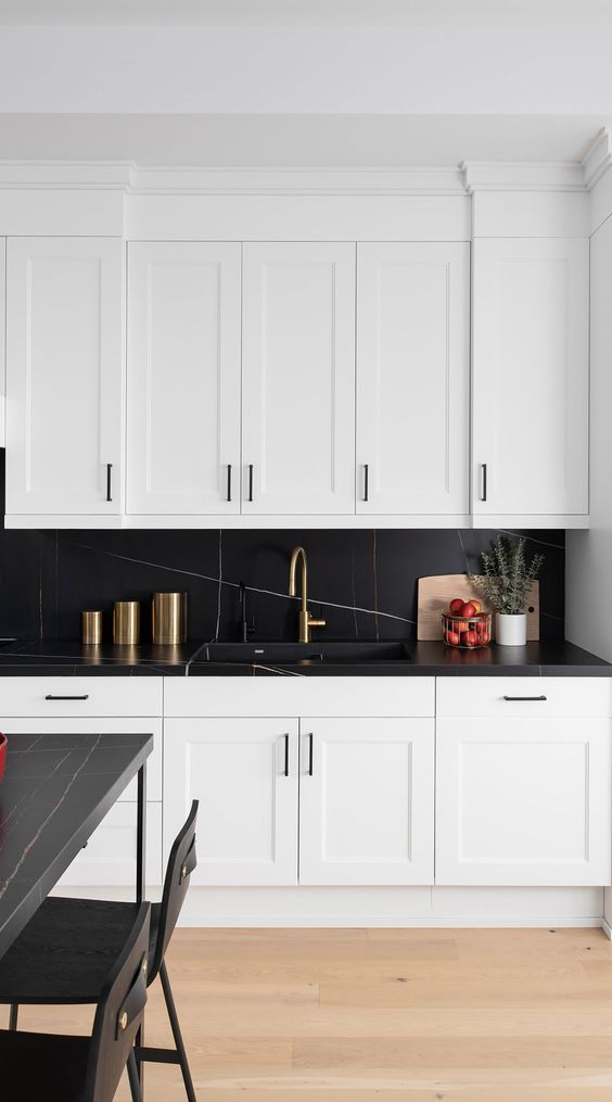 a refined kitchen with white shaker cabinets, a chic black marble backsplash and countertops, a black table and chairs