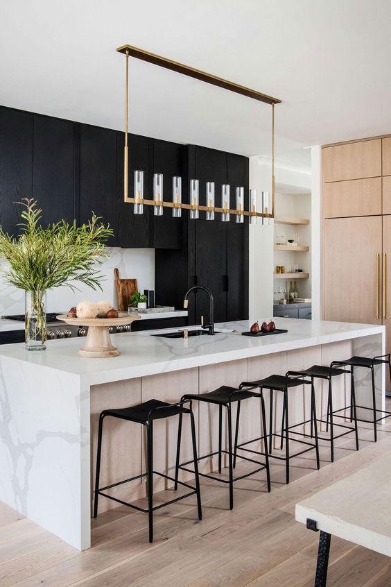 a refined modern kitchen with matte black cabinets, a white kitchen island with a white stone countertop, a chic chandelier and black fixtures