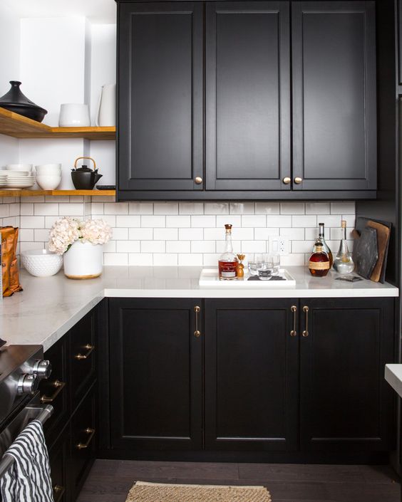 a rustic meets modern kitchen with black shaker cabinets, white stone countertops and a white tile backsplash, brass fixtures