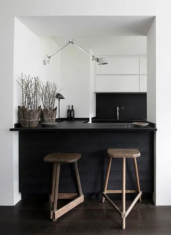 a small minimal black and white kitchen with a kitchen island and dining space in one, with mismatching wooden stools and a white lamp