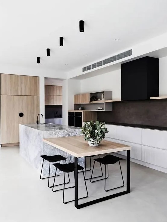 a stylish contemporary kitchen with white lower cabinets, open storage shelves, a black hood, black countertops, light stained wood and a stone kitchen island