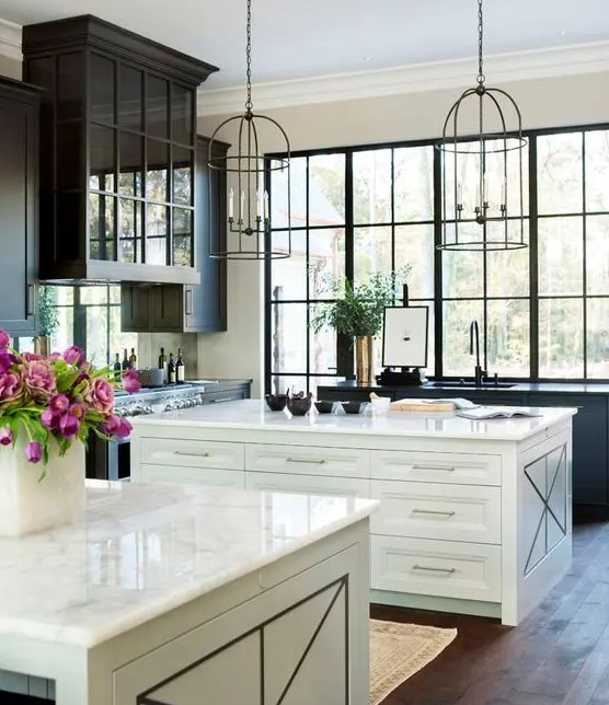 an elegant vintage kitchen with black cabinets and two white kitchen islands, cage-like pendant lamps and a large window to enjoy the view of the garden
