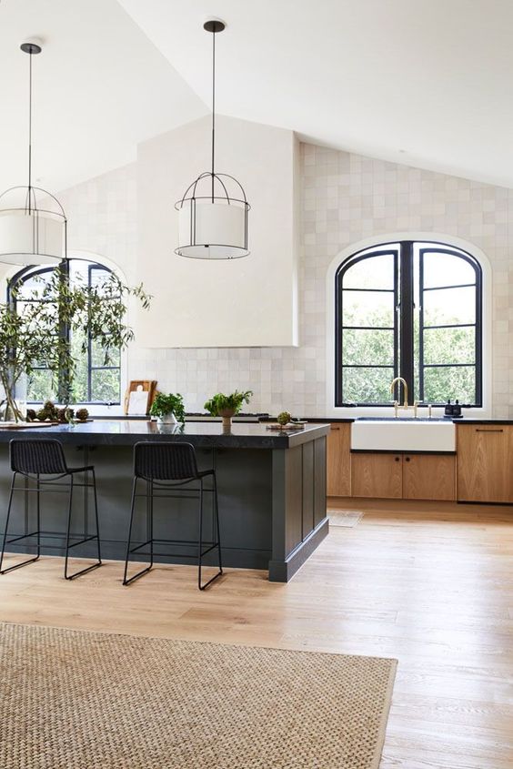 an elegant vintage kitchen with stained cabinets, a black kitchen island, a white hood and arched window with black frames