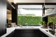black wooden cabinets look great with white marble tops and make a perfect contemporary kitchen, and a window with a greenery view fills the space with light