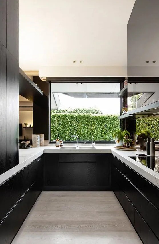 black wooden cabinets look great with white marble tops and make a perfect contemporary kitchen, and a window with a greenery view fills the space with light