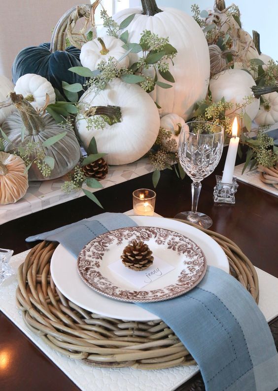 a Thanksgiving table with velvet and natural pumpkins, greenery, pinecones, a woven charger and blue napkins