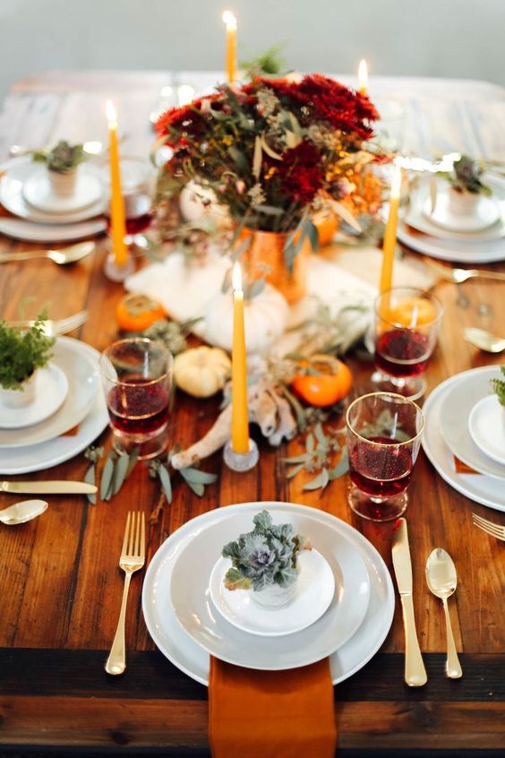a bold rustic Thanksgiving table with rust napkins, pumpkins, greenery, a bold floral arrangement and bright candles