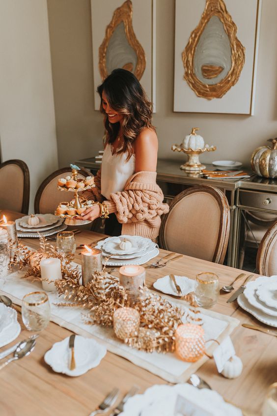 a gold and white Thanksgiving tablescape with candles, wooden candleholders, gilded leaves and elegant white porcelain