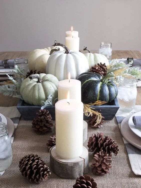 a neutral Thanksgiving centerpiece of green pumpkins, candles and pinecones is a great idea for a rustic tablescape