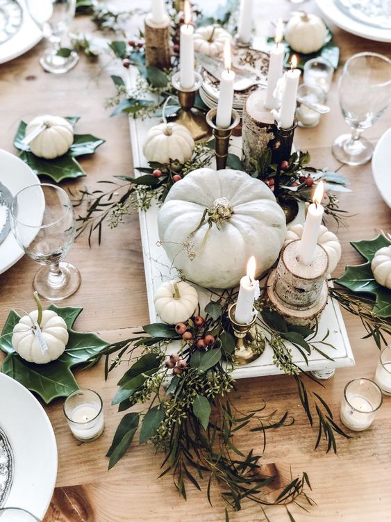 a neutral Thanksgiving table with white pumpkins, leaves, berries, candles and tree stumps and slices is very cool
