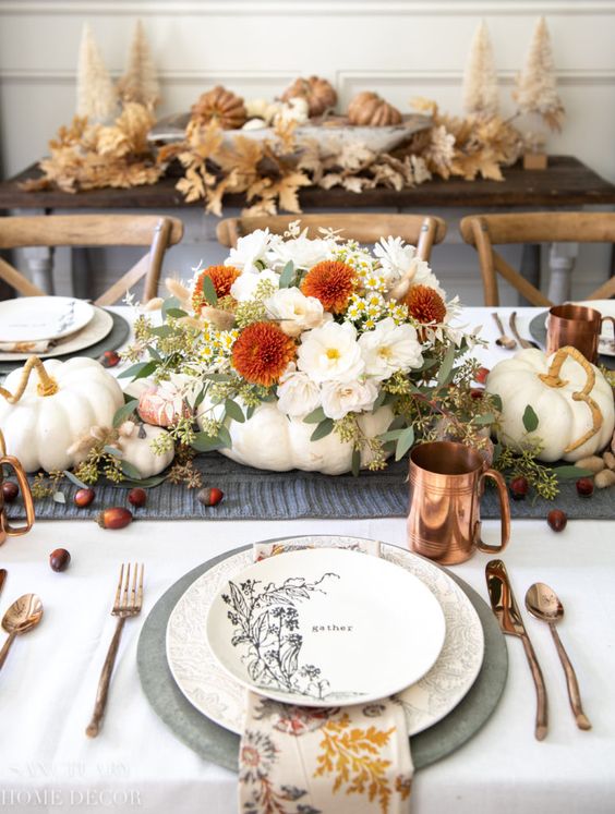 a neutral modern farmhouse Thanksgiving tablescape with a grey runner and chargers, printed plates, napkins and a pumpkin with neutral and bold blooms, copper mugs and cutlery