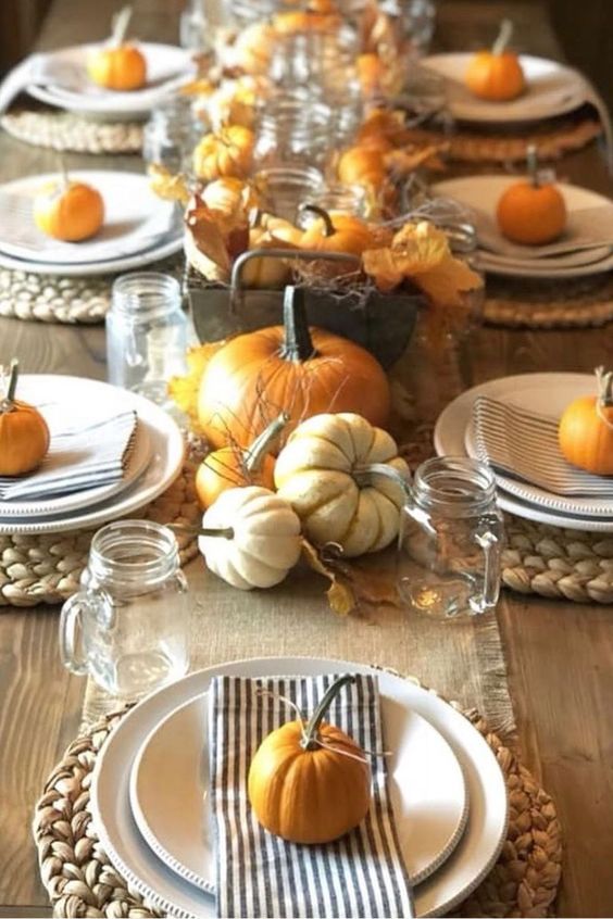 a pretty rustic Thanksgiving table with striped napkins, a burlap runner, orange and white pumpkins, jar mugs and leaves