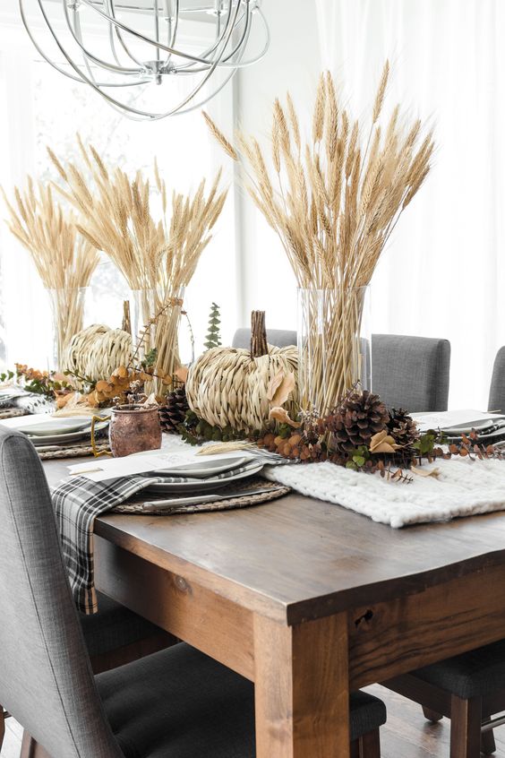 a rustic fall or Thanksgiving tablescape with a knit runner, pinecones, woven pumpkins, greenery and wheat is love