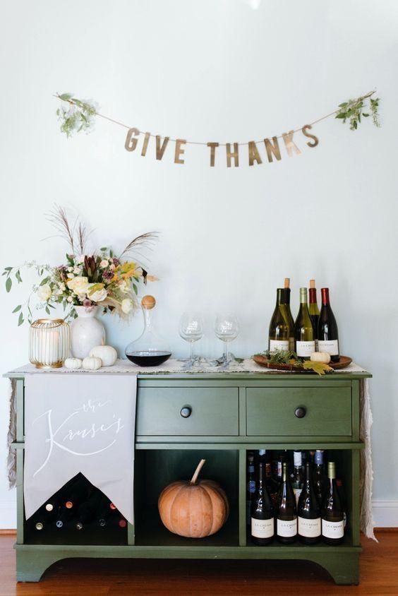 a simple Thanksgiving bar with a gold banner, pumpkins and a bold floral arrangement is a gorgeous idea
