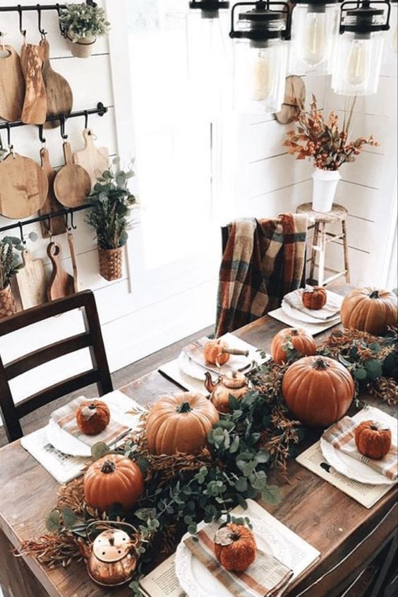 a simple rustic Thanksgiving table with a lush greenery runner, orange pumpkins and gourds, copper teapots and mugs