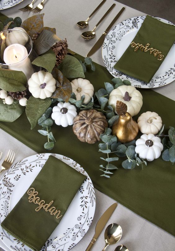 a stylish Thanksgiving tablescape with green linens, pumpkins, greenery and candles plus printed plates