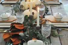 a vintage rustic Thanksgiving tablescape with a greenery and magnolia leaf runner, candles, pears, square plates and striped linens