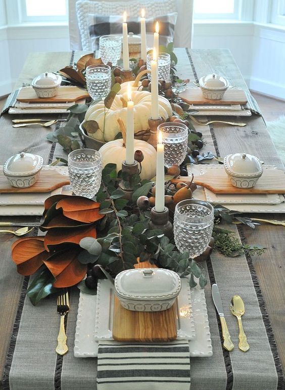 a vintage rustic Thanksgiving tablescape with a greenery and magnolia leaf runner, candles, pears, square plates and striped linens