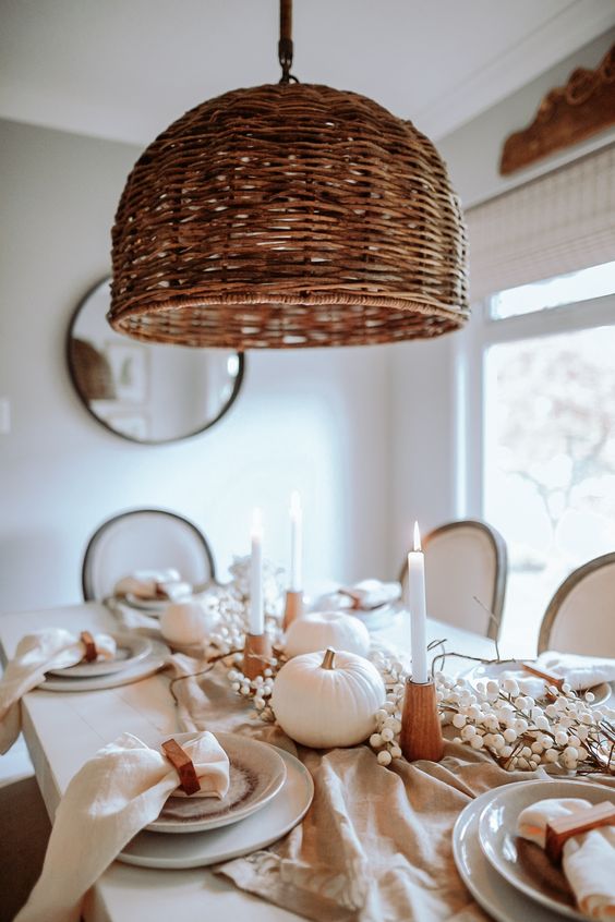 an ethereal white Thanksgiving tablescape with berries, pumpkins, elegant porcelain and linens, candles in wooden candleholders