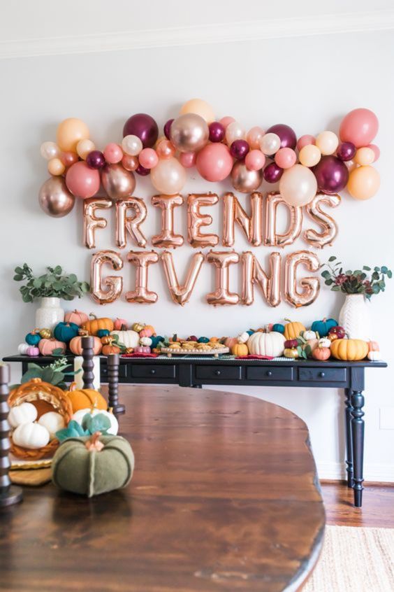 bright Thanksgiving decor with bold pumpkins of various sizes, greenery, bold ballons and balloon letters over the table