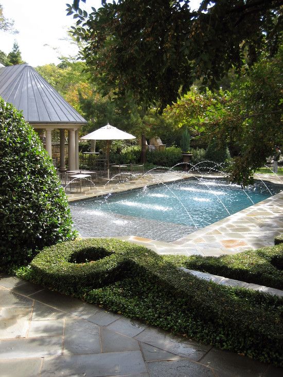 a cool and elegant outdoor space with a pool, fountains, greenery and trees and a cabana plus a dining space
