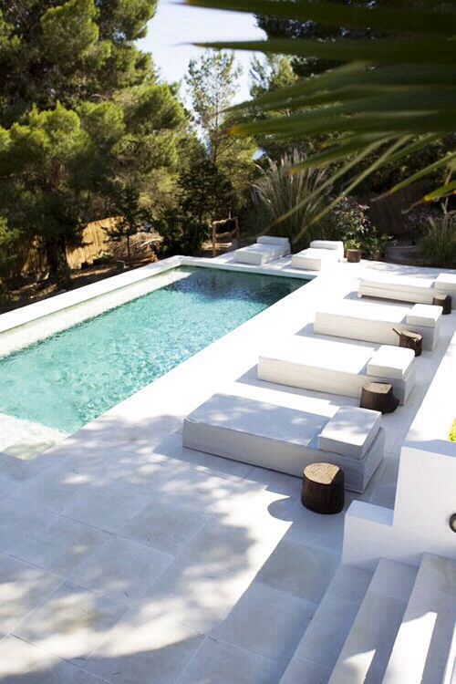 a minimalist backyard with a pool, antislip stone tiles that form a deck and steps, a series of loungers with stump side tables