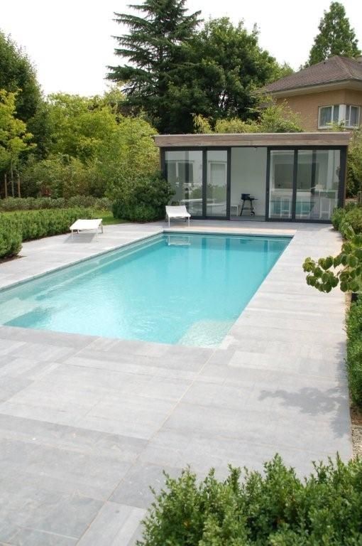 a minimalist outdoor space with a blue pool, neutral stone tiles, some white loungers and greenery around is amazing