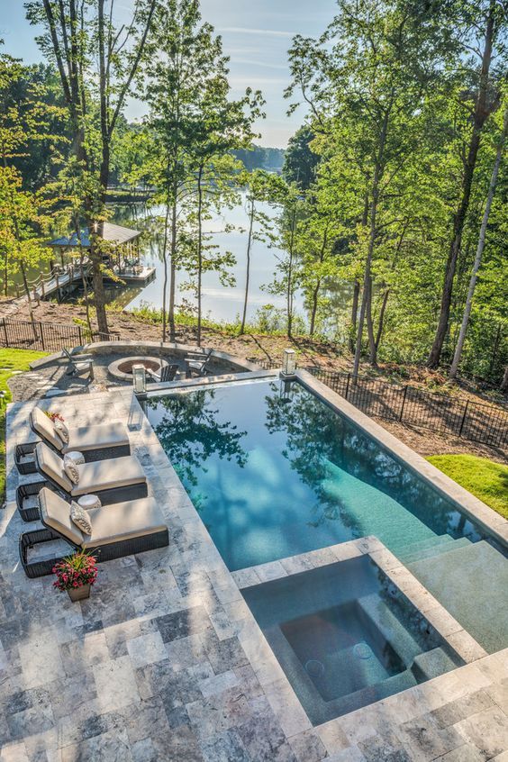 a modern and welcoming outdoor space with a pool and a jacuzzi, a stone deck and wicker loungers plus a view of the lake