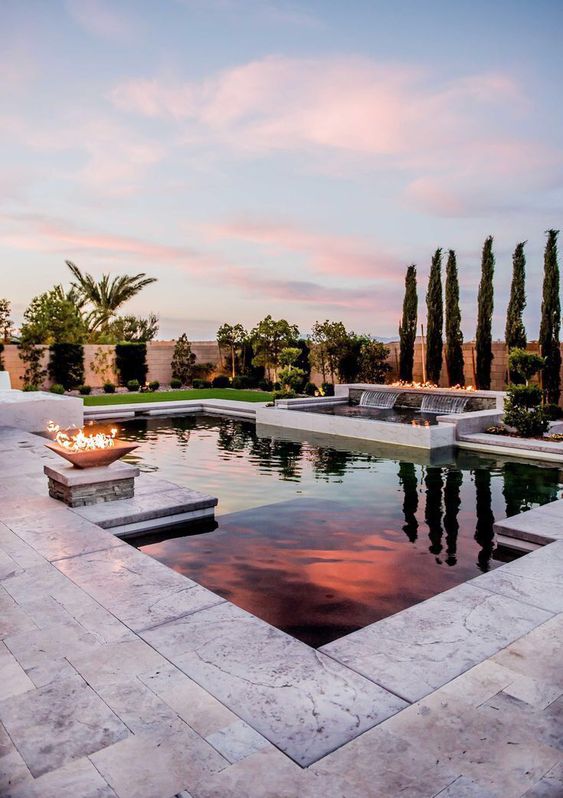 a neutral outdoor space with a geometric pool, white stone tiles, a fire pit and a waterfall is a very spectacular and cool space