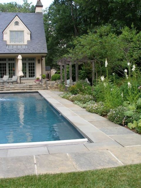a welcoming outdoor space with a pool with a stone deck, greenery and blooms around and green lawn is very stylish