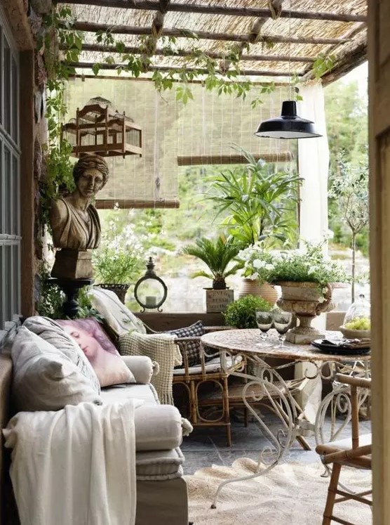 a Provence-inspired outdoor living room with rattan and metal furniture, neutral and pastel textiles, potted greenery and blooms and some pendant lamps