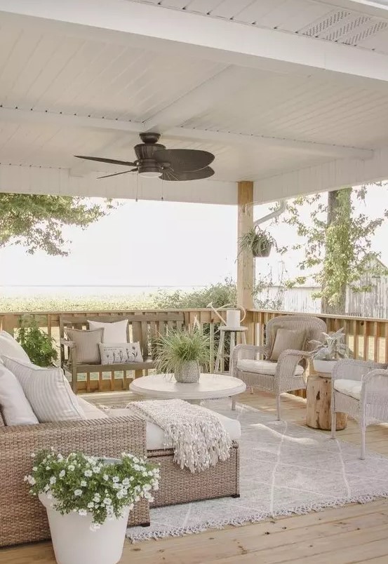 a beautiful neutral farmhouse outdoor living room with neutral wicker furniture, a round coffee table, potted plants and blooms
