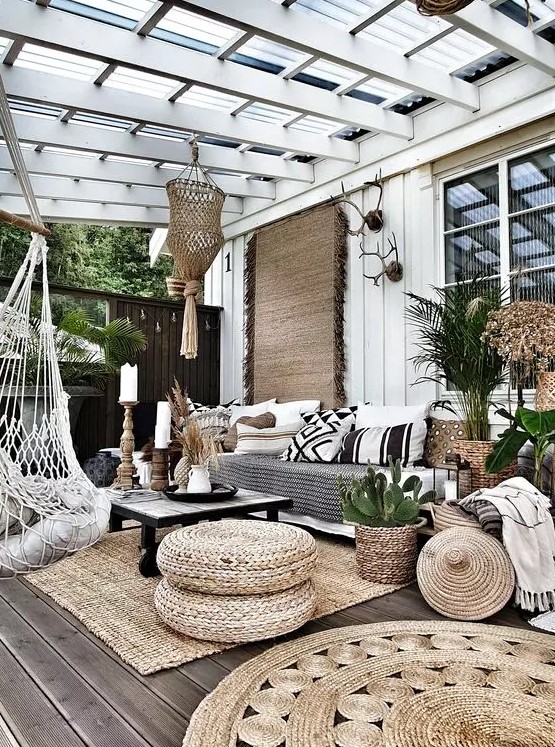 a boho outdoor living room with a jute rug and poufs, a sofa with black and white pillows, a low black table and a pendant chair