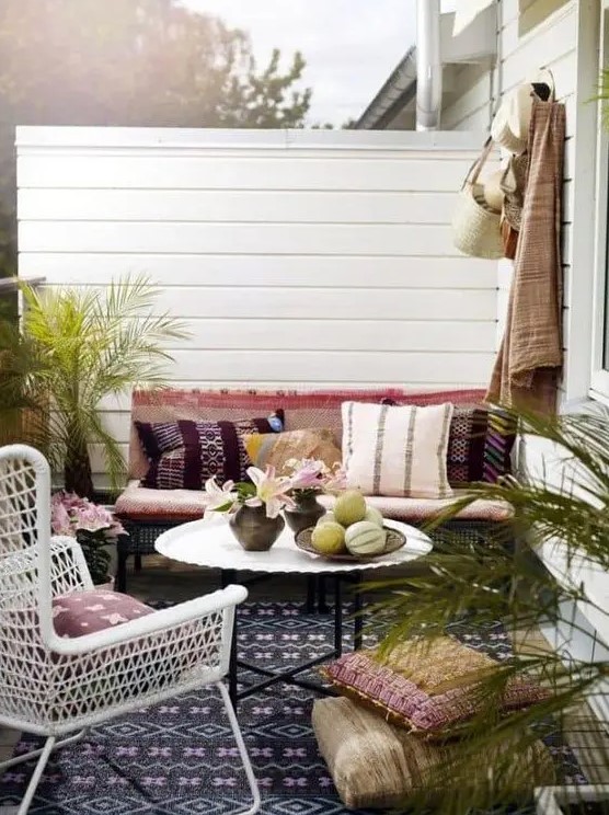 a boho outdoor living room with colorful textiles and rugs, potted greenery and a white wicker chair