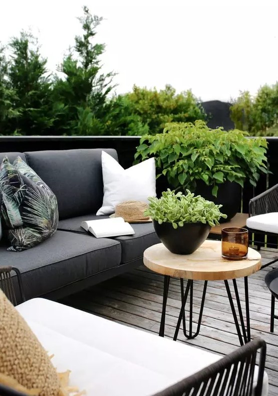 a cool Scandinavian outdoor living room with a grey sofa, white and black chairs, a hairpin leg coffee table and potted greenery