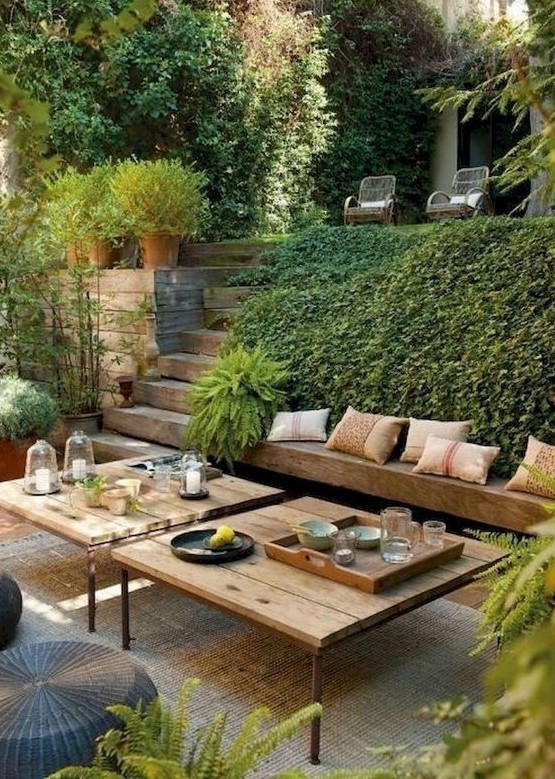a modern Mediterranean outdoor living room with a built-in bench, modern furniture, wicker ottomans and lots of greenery