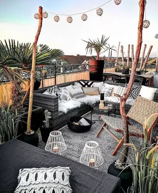 a monochromatic summer outdoor living room with black furniture, black and white textiles, candle lanterns and potted greenery and trees