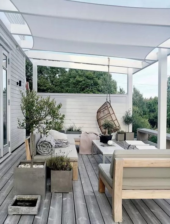 a neutral Scandinavian outdoor living room with olive green upholstered furniture, folding chairs and a coffee table, a pendant chair and potted plants