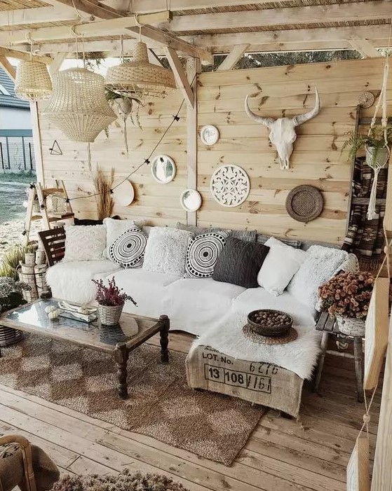 a neutral boho outdoor living room with a white corner sofa, a low coffee table, a gallery wall with mirrors and skulls and wovne pendant lamps