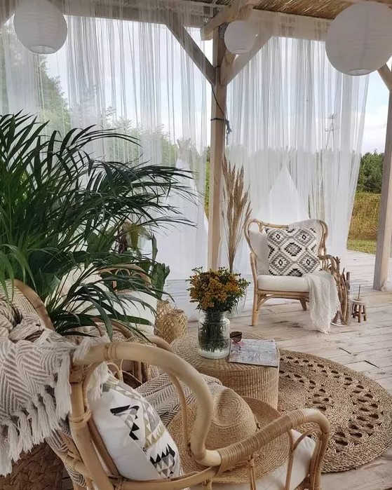 a neutral boho outdoor living room with rattan chairs, black and white pillows, potted greenery and paper pendant lamps