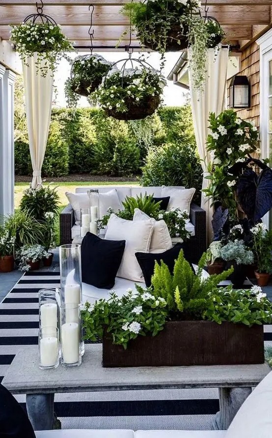 a stunning black and white outdoor living room with black wicker furniture, a stone bench, lots of greenery, blooms and candles