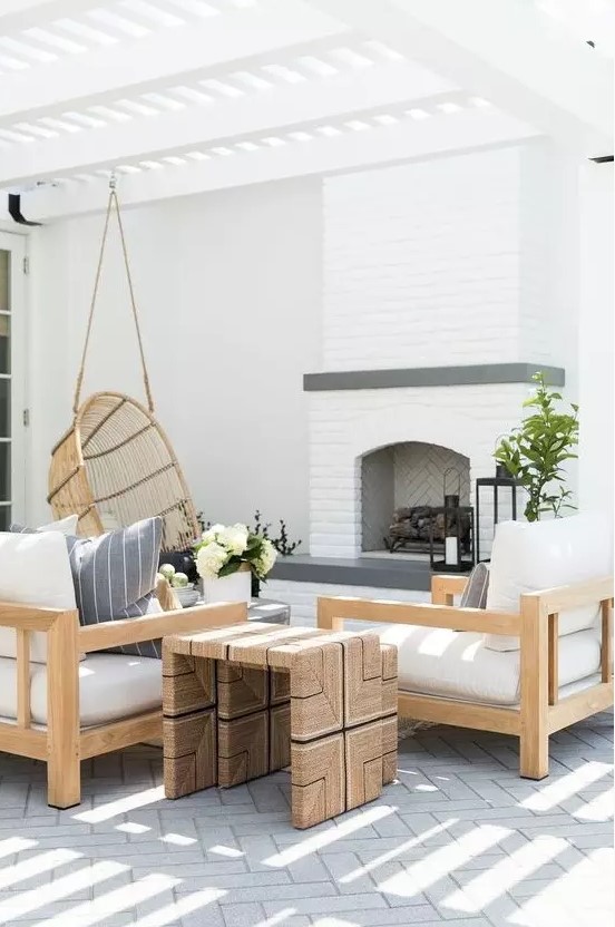 a welcoming modern farmhouse outdoor living room with a fireplace, neutral upholstered furniture, a duo of side tables and a pendant chair