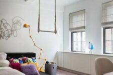 a bright teen girl bedroom with a black platform bed, a hot pink pendant lamp, colorful bedding, simple shades is welcoming