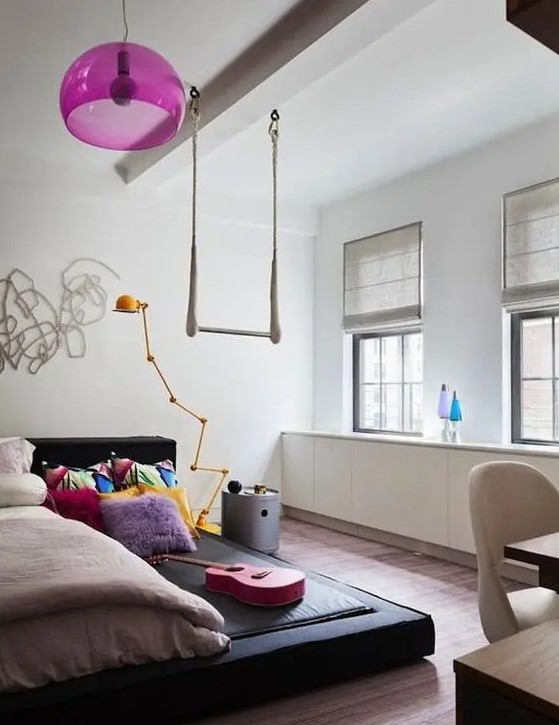 a bright teen girl bedroom with a black platform bed, a hot pink pendant lamp, colorful bedding, simple shades is welcoming