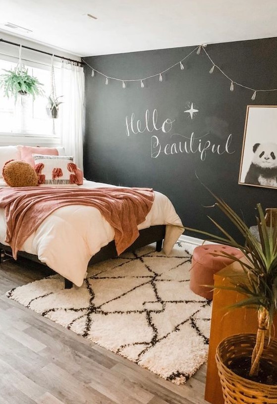 a chic teen bedroom with a chalkboard wall, a bed with pretty pink bedding, a wooden desk, a chair and a footrest