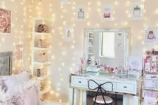 a glam teen bedroom with a grey bed with pink and blue bedding, a white desk and a mirror, a crystal chandelier and a shelf in the corner