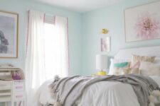 a lively teen girl bedroom with aqua walls, a white bed with printed pillows, white poufs, a white desk and a chair, a gold chandelier